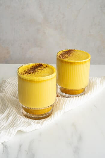 Two glasses of golden milk topped with cinnamon, made from coconut, turmeric, and ginger. 