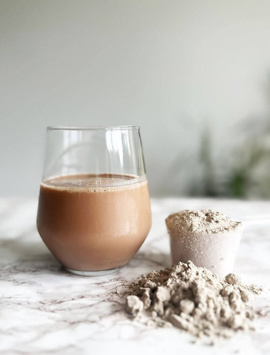 Glass of chocolate oat milk with powdered cocoa on a white surface